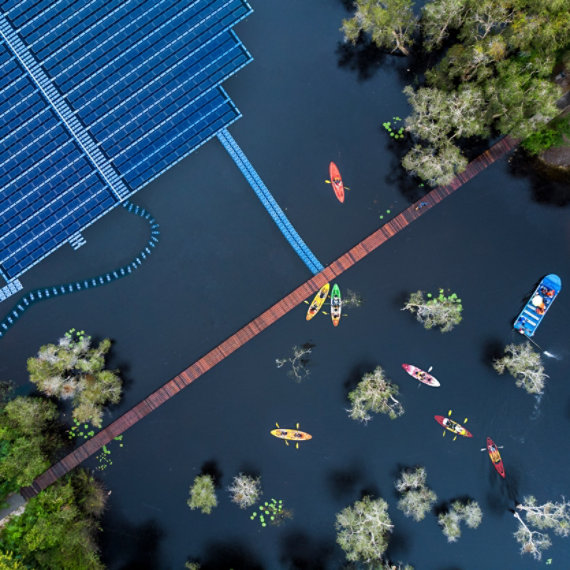 Aerial view of floating solar cells for clean energy alongside people in small colorful kayaks and a blue flat bottom boat.