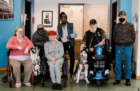 A group of people, some in wheelchairs, posing together indoors with a service dog.