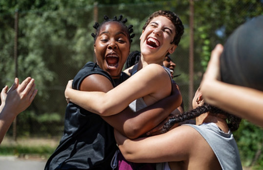 Three women hugging and laughing on a basketball court